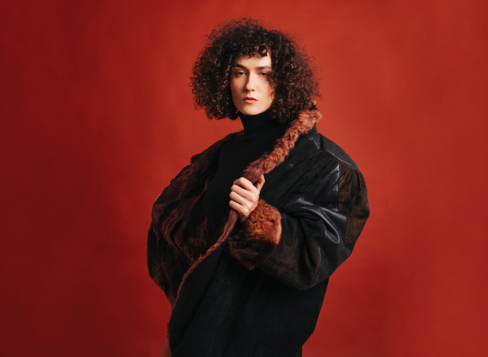 A tall woman with leather jacket in front of a red background