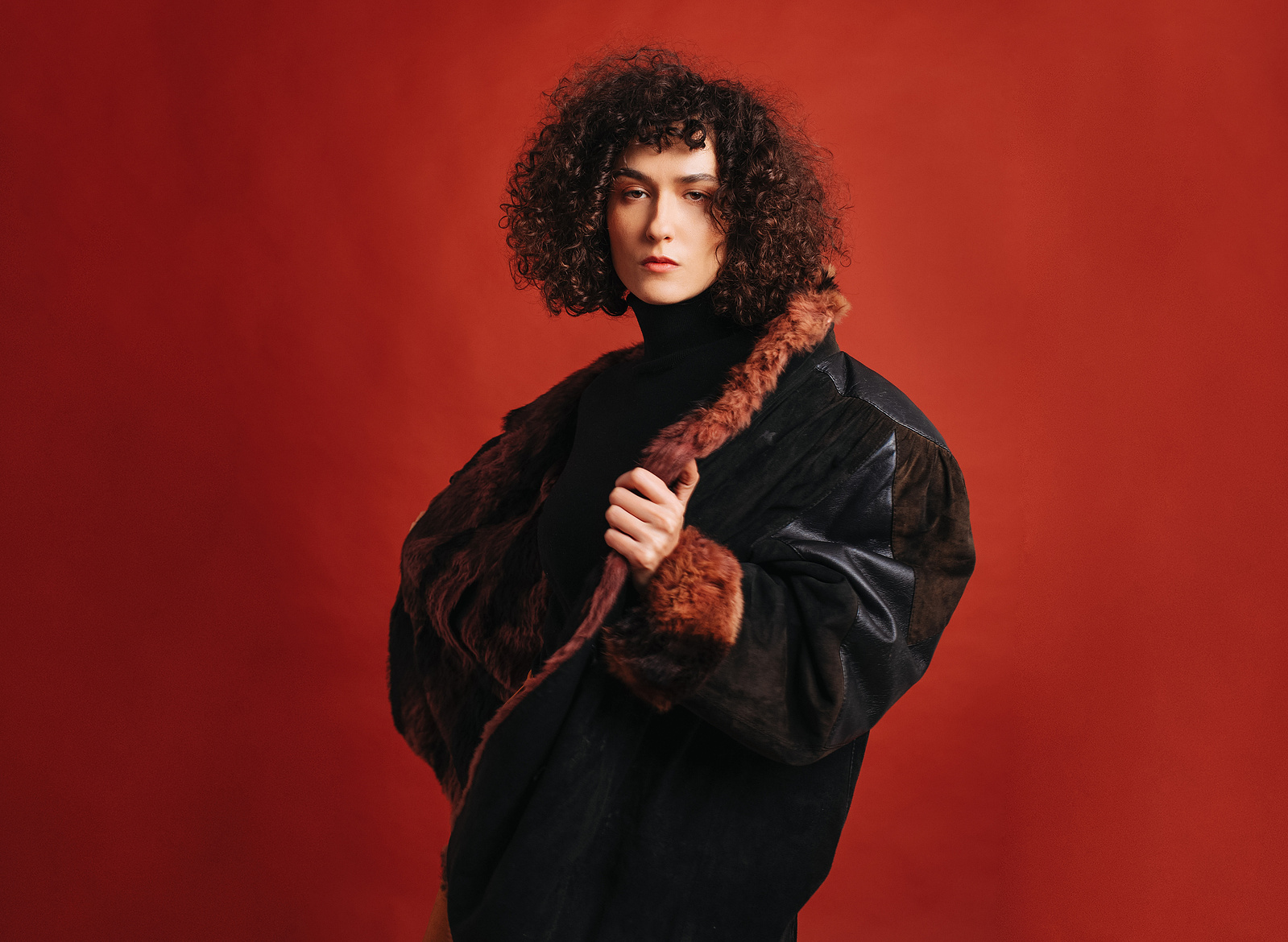 A tall woman with leather jacket in front of a red background
