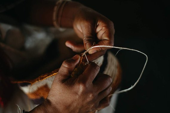 close up of hands knitting a backpack with thread and needle 