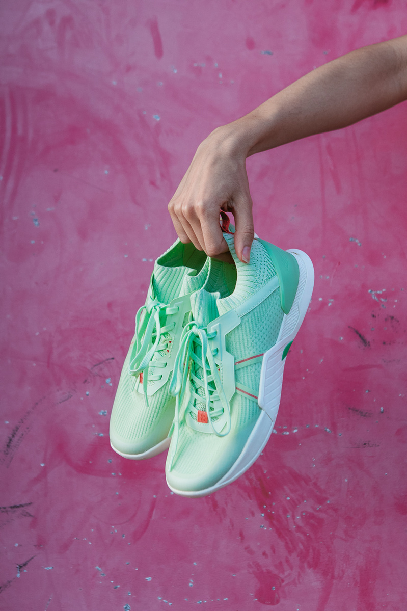 hands holding green shoes on a pink background with pink paint.