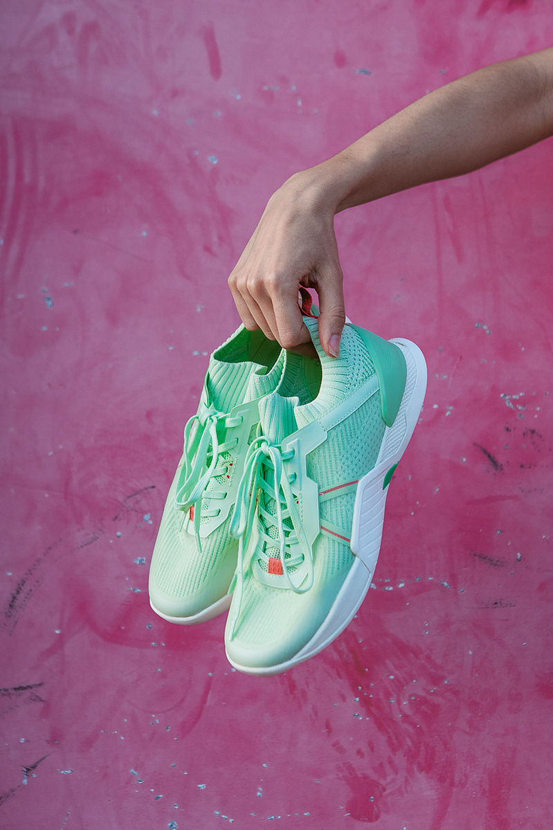 hands holding green shoes on a pink background with pink paint.
