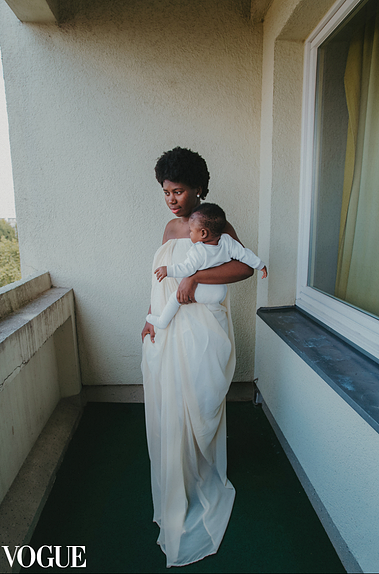 An African American woman in a white dress holding her baby