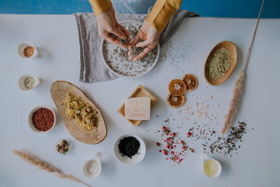 hands preparing a recipe over a bowl with lots of herbs around it 