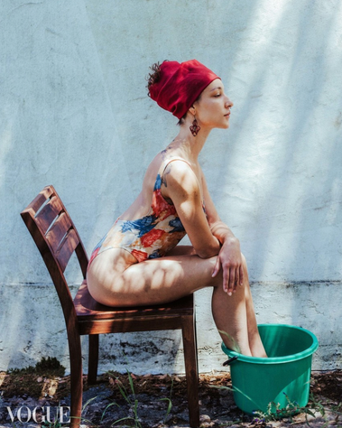 Woman sitting on a chair with a red tie on her head, her bathing dress of flowers, and her feet in an green bucket.