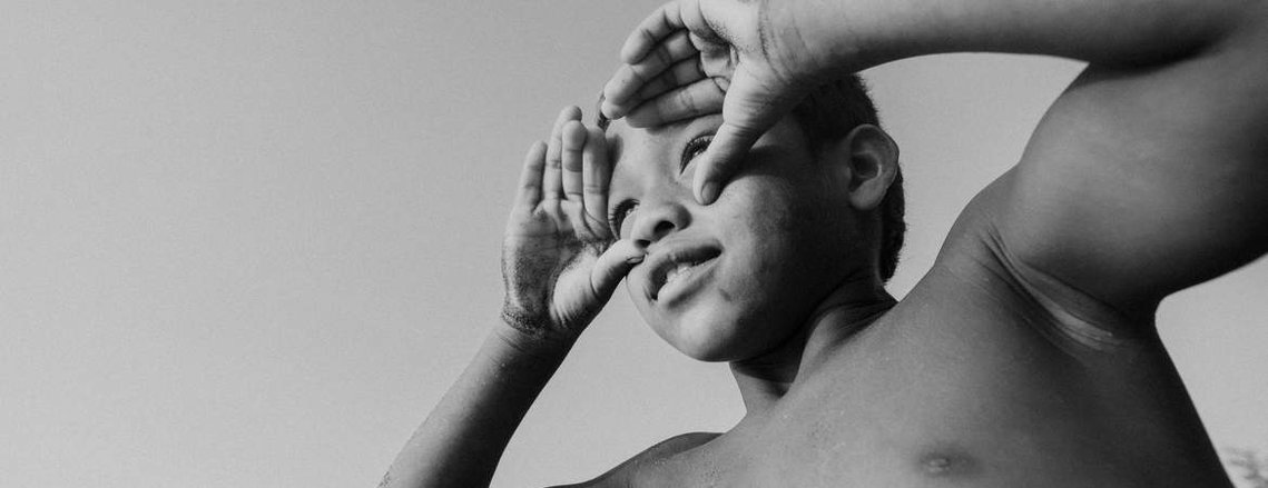 child with his hands on his face looking at the horizon
