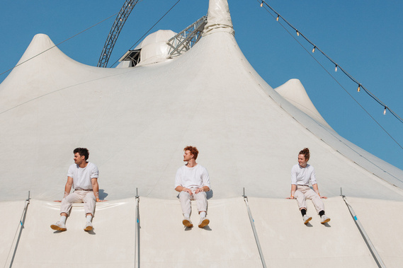 three circus performers dressed in white seated on top of circus tent