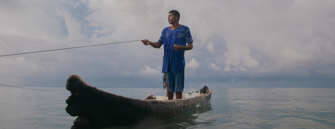 Fisherman fishing in his boat, with his blue clothes and net in his hands.