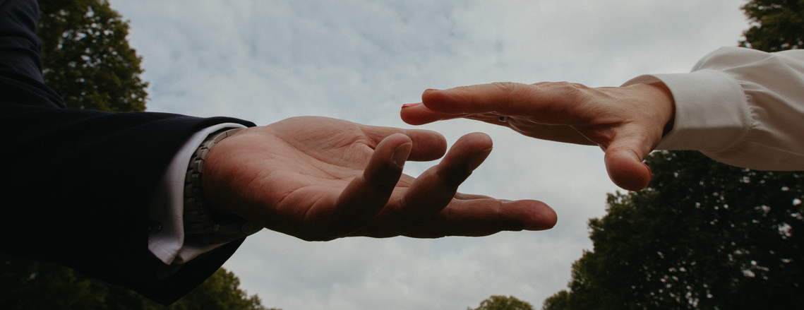 close up of hands about to touch against a sky background 