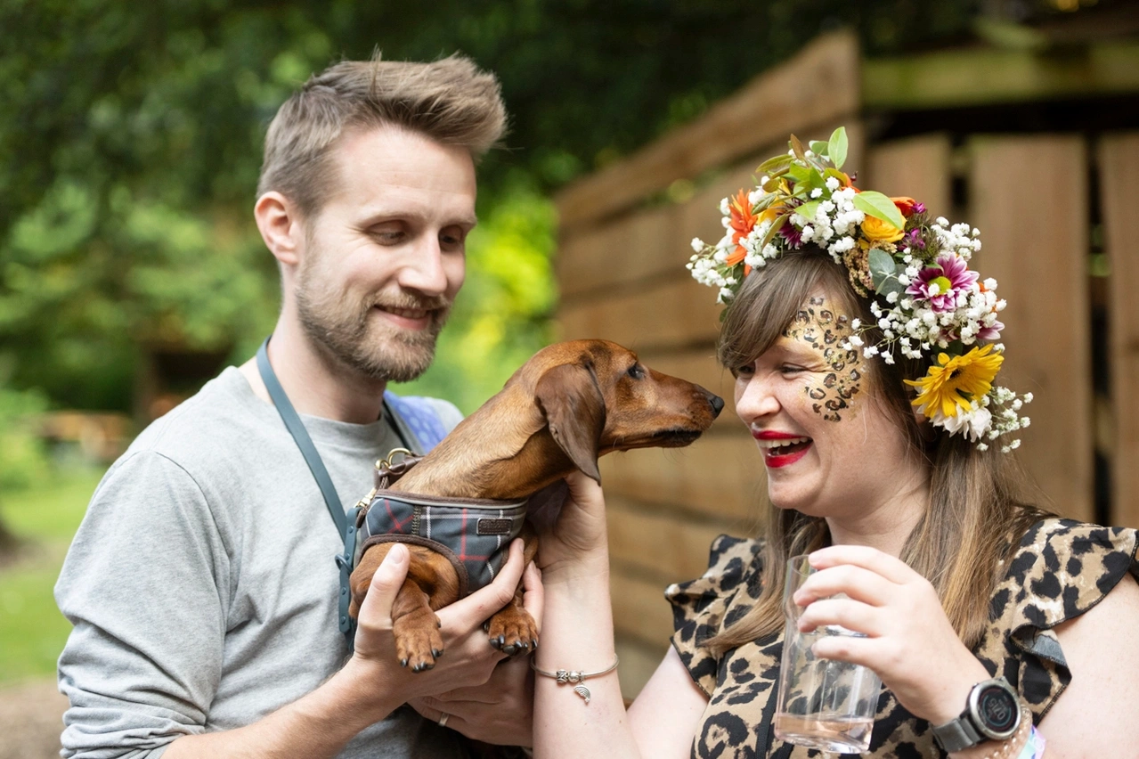 Couple with puppy playing trying to lick girls face festival scene taken of Box Clever consulting at Hazlewood Castle photographed by Mark Wheelwright from Aire Street Studios Leeds