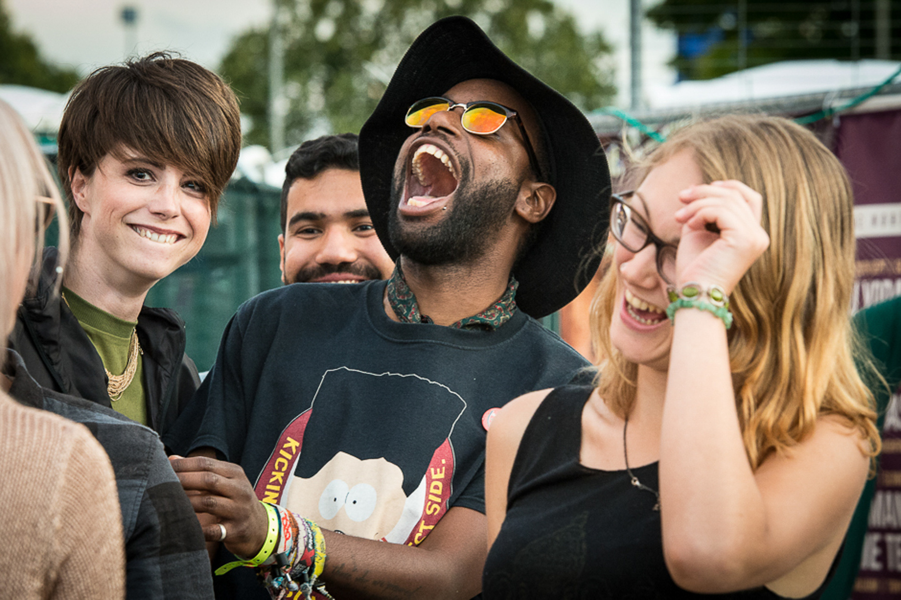 Young black man wearing shades laughing with 2 young cool white girlfriends at a festival photographed by Mark Wheelwright from Aire Street Studios Leeds