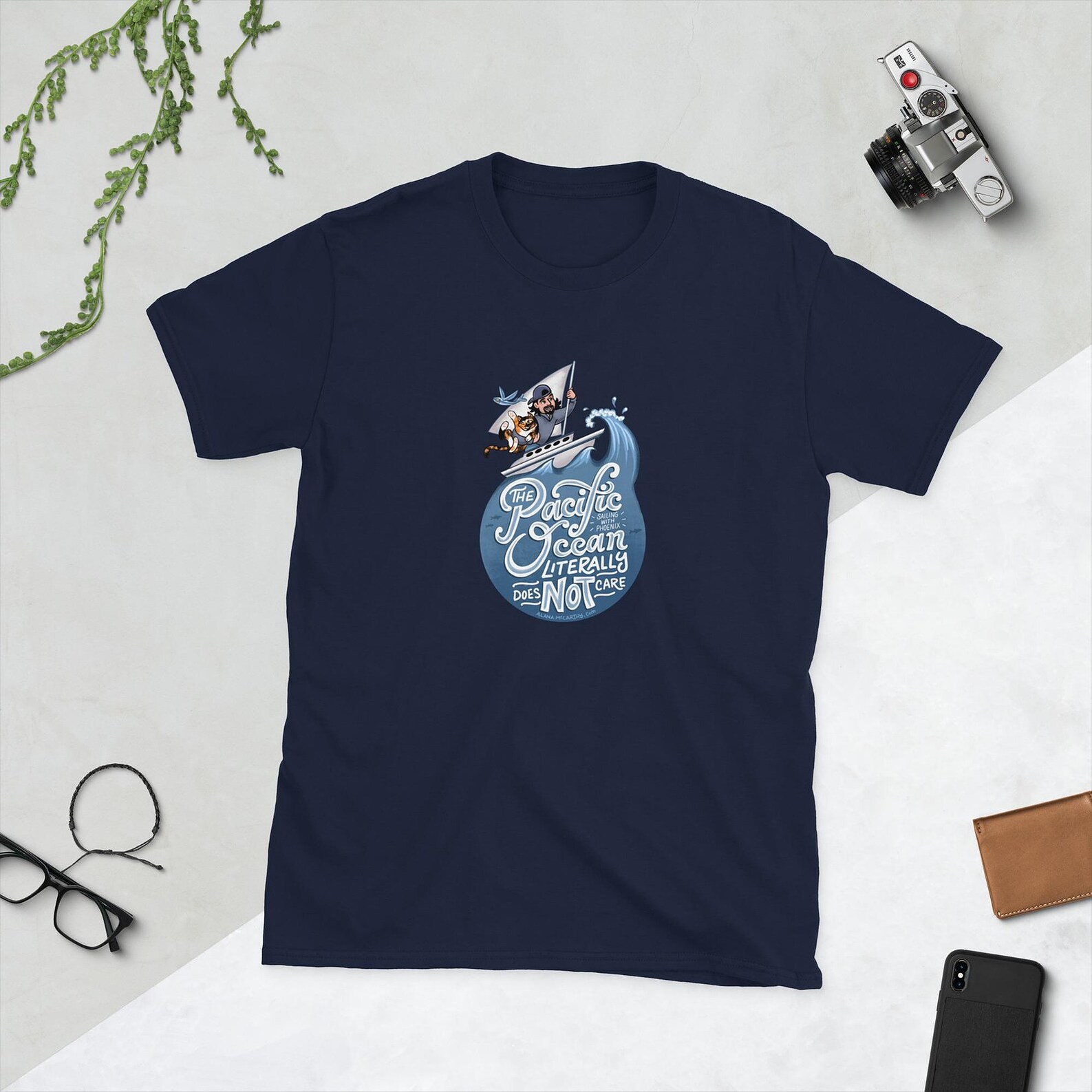 T-Shirt design. Sailing with Phoenix, man and his cat on a sailboat crashing through ocean waves. The cat is swiping at a flying fish. Hand lettered text reads "The Pacific Ocean Literally Does Not Care"