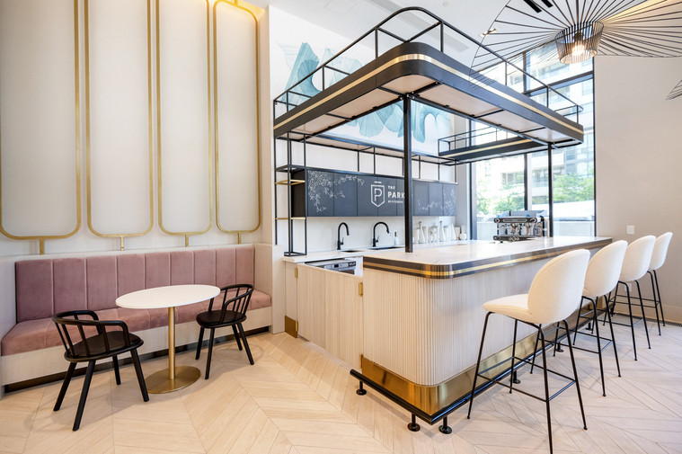 Stylish modern minimalist condo lobby decorated in gold, pink and teal. Wine and coffee marble bar with stools. Chalk drawing of The Parker logo with leafy vines drawn on the chalk board cabinets behind the bar.