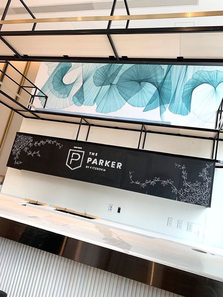 Detail of the chalkboard drawing by Alana McCarthy on the cabinets behind the marble coffee bar. Leafy vines surround The Parker by Fitzrovia logo under a modern teal artwork.