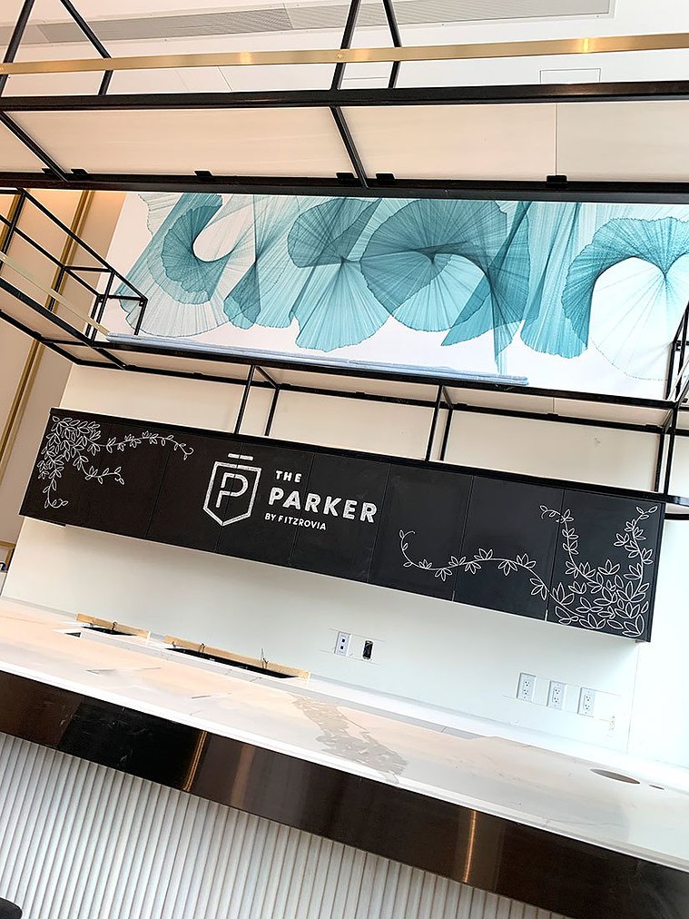 Detail of the chalkboard drawing by Alana McCarthy on the cabinets behind the marble coffee bar. Leafy vines surround The Parker by Fitzrovia logo under a modern teal artwork.