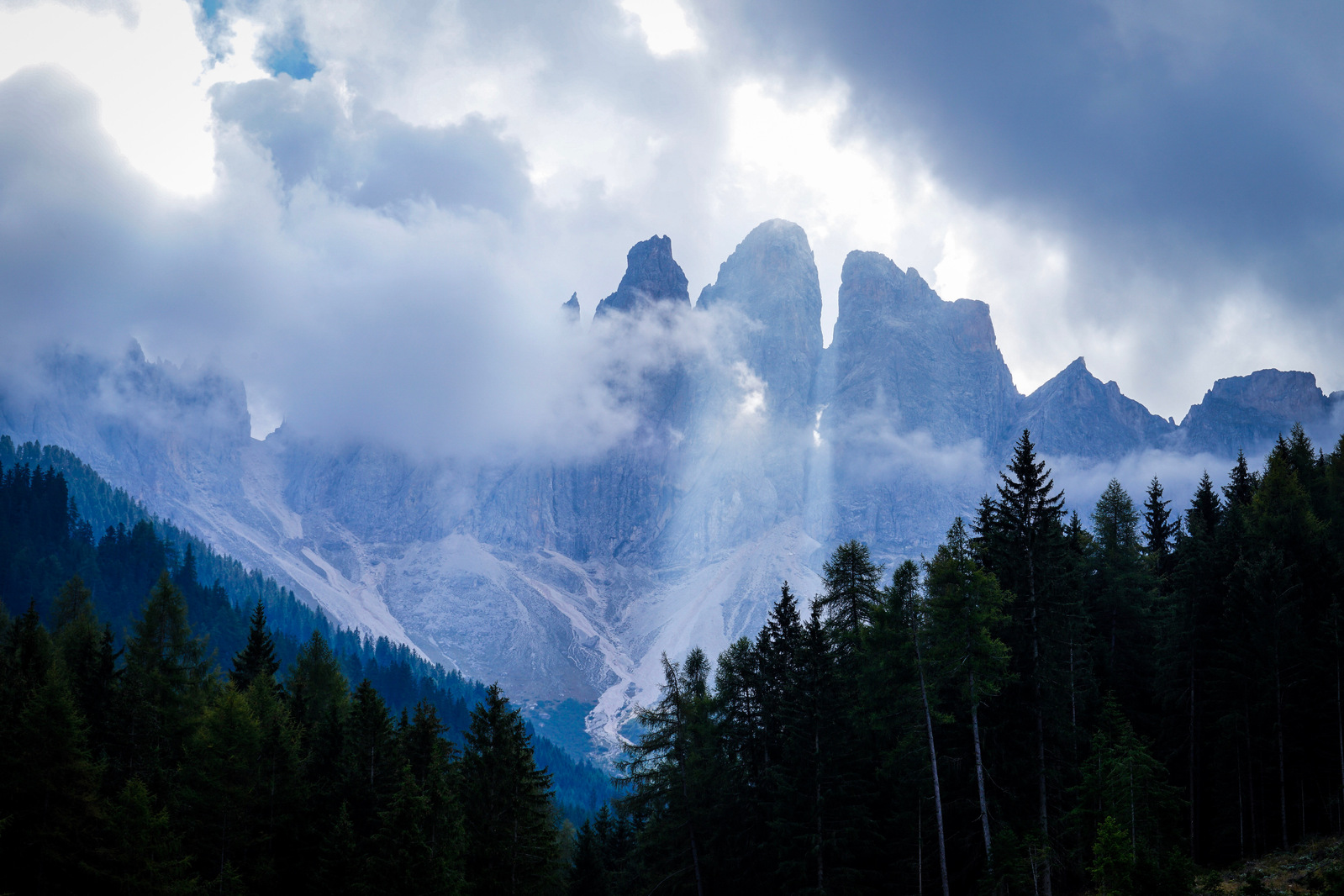 The sharp edge of tall rocky mountains emerges from low clouds. 