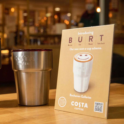 Costa Burt Campaign Tent Card stood next to metal Costa reusable cup on table in Costa restaurant