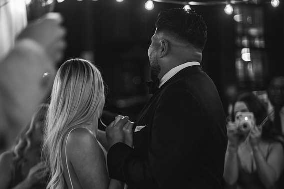 couple dancing under fairy lights at wedding while friends look on black and white film photography