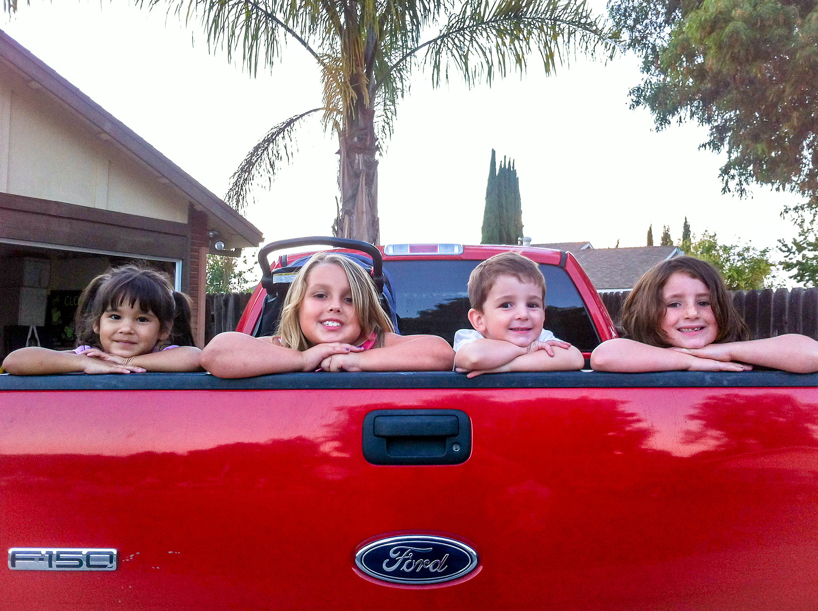 4 kids smiling inside a red truck. portrait photography