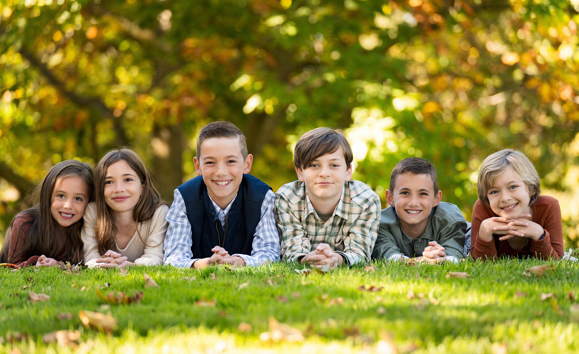 Group of children laying on their stomachs smiling and then making faces to the camera.
