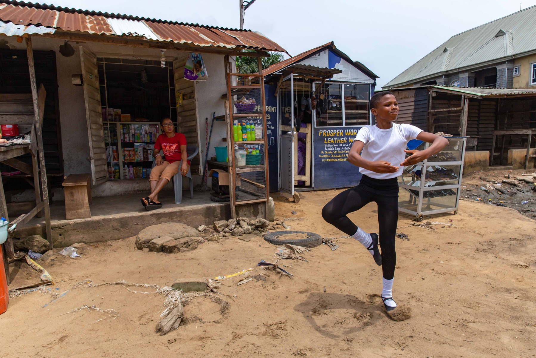 A student of the Leap of Dance Academy, Anthony Madu Mmesoma performs a ballet dance routine in front of his mother's shop while his mother sits and watches him at Okelola street, Ajangbadi in Lagos on July 3, 2020. Leap of Dance Academy is a ballet dance