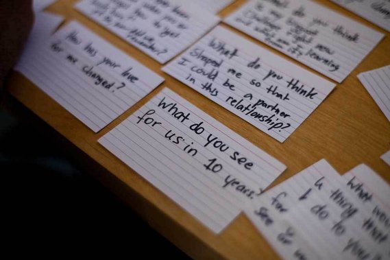 index cards on a wooden table with handwritten questions, the one in focus reading 