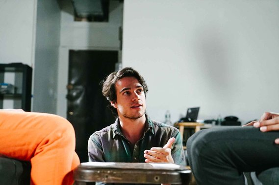Nick kneels in front of two people sitting, but out of frame, speaking to both of them