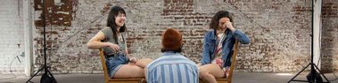 Nick sits in front of two women sitting across from each other on wooden chairs, laughing together