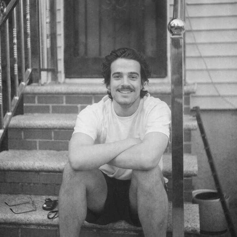 Nick sitting on porch steps, smiling at camera, black and white