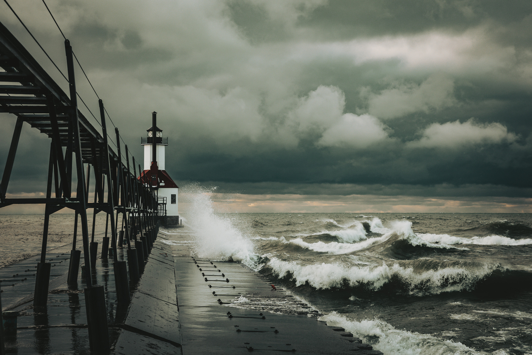 Waves crash against the pier at the St. Joseph North Pier Lighthouse on Lake Michigan under stormy skies.