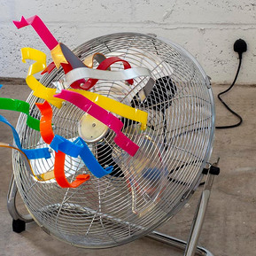 Acrylic ribbons attached to a fan that is off with the plug directly in the wall