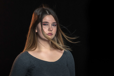 A young girl with long hair blowing in the wind wearing a green top on a black background.