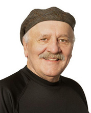 A headshot portrait of a man with grey hair and a mustache wearing a black shirt and backward flat cap all on a white background.
