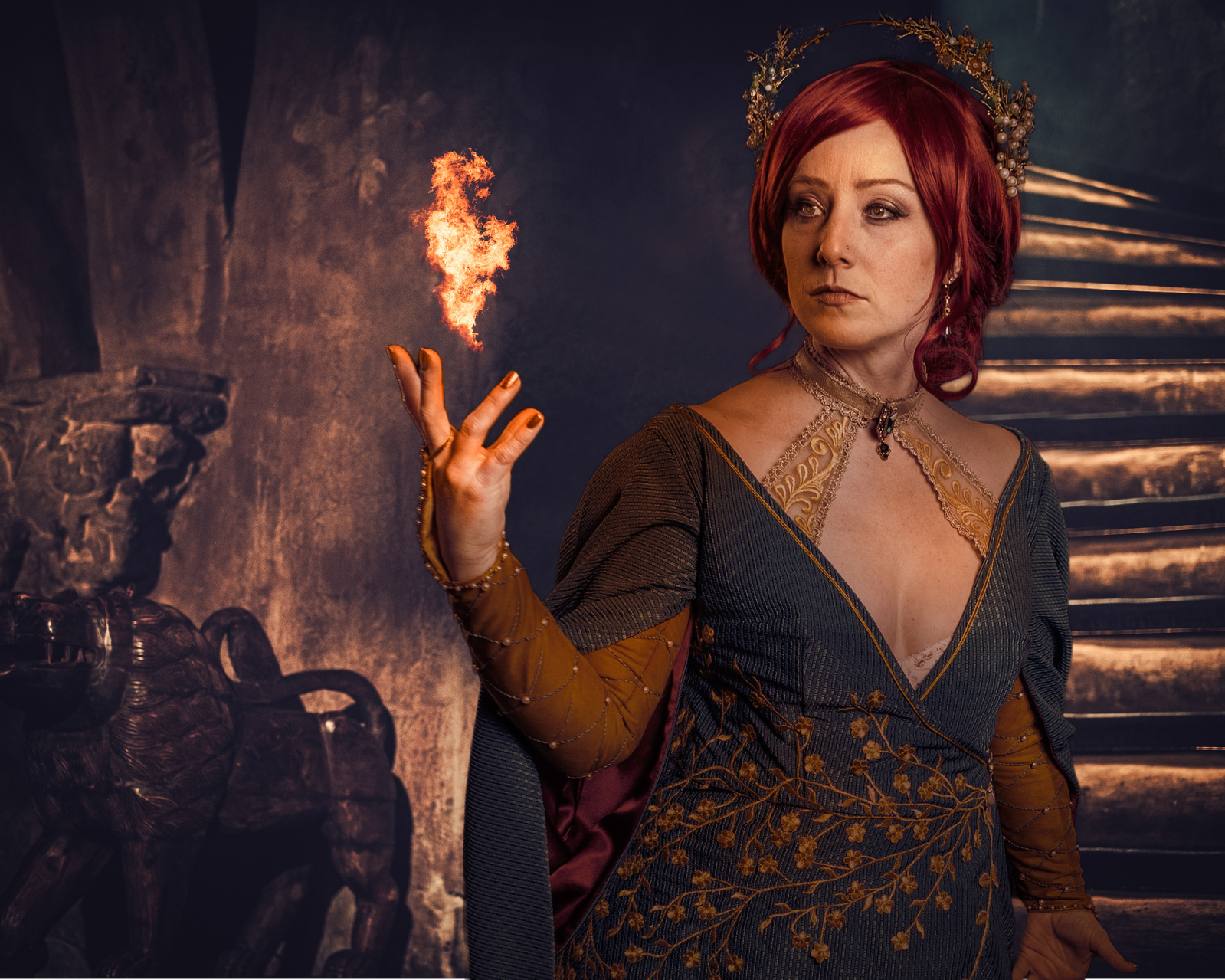A digital artistry image and a magical scene of a woman with red hair and green and gold dress with her hand up from which extends a flame