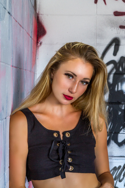 Portrait of an attractive blonde woman in a black tank top against a wall of graffiti.
