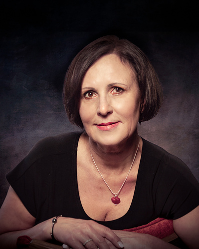 A portrait of a lady with dark hair and a black dress leaning forward over her arms all against a dark background.