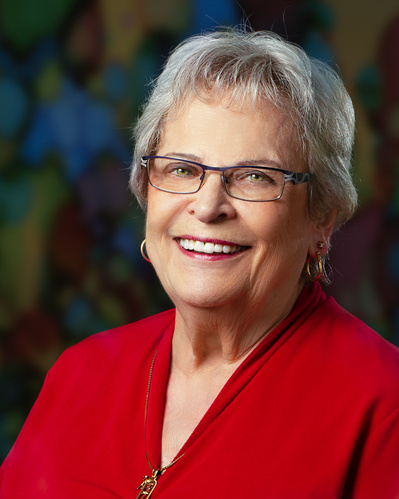 A portrait of an older woman wearing glasses and a red dress with a wonderful smile on her face all against a darker but colorful background