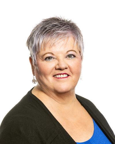 A headshot portrait of a woman with short great hair wearing a black sweater over a blue top against a white background.