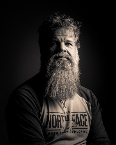 A monochromatic headshot of a man with long beard on a dark background