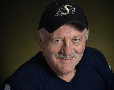 A portrait of a photographer wearing a black cap and dark blue hockey jersey on a dark background