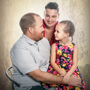 A creative family portrait of a father holding his daughter on his knee and a mother  looking at each other.
