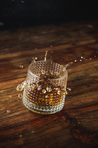 8 Rivers Rum X Scott Uzoho -- product still-life photography of glass of whiskey in spinning motion spilling out from the glass on a wooden table 