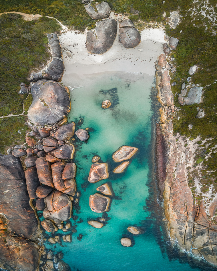 A bird's eye view of a sheltered beach with large rock formations in and around the water.