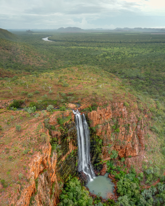 A large waterfall on the edge of a 70 metre high escarpment. Rolling green hillsides in the distance.