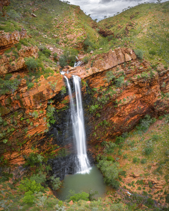 A large waterfall amongst green hillsides and a steep sandstone escarpment.