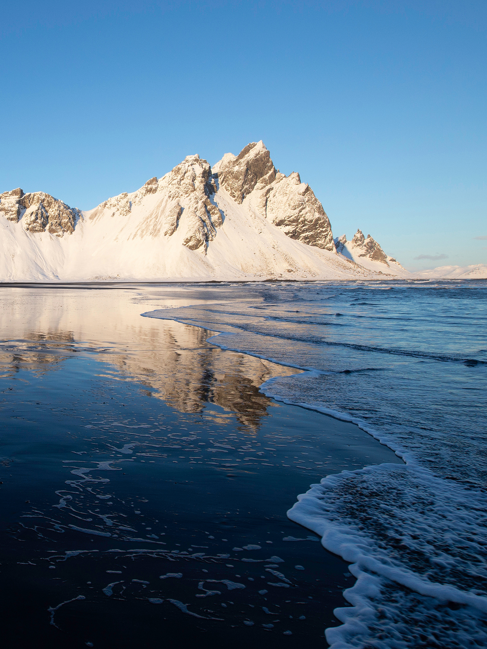 The magnificent Vestrahorn Mountain in Iceland is reflected on the wet black sand beach on a winter afternoon. (Portrait)