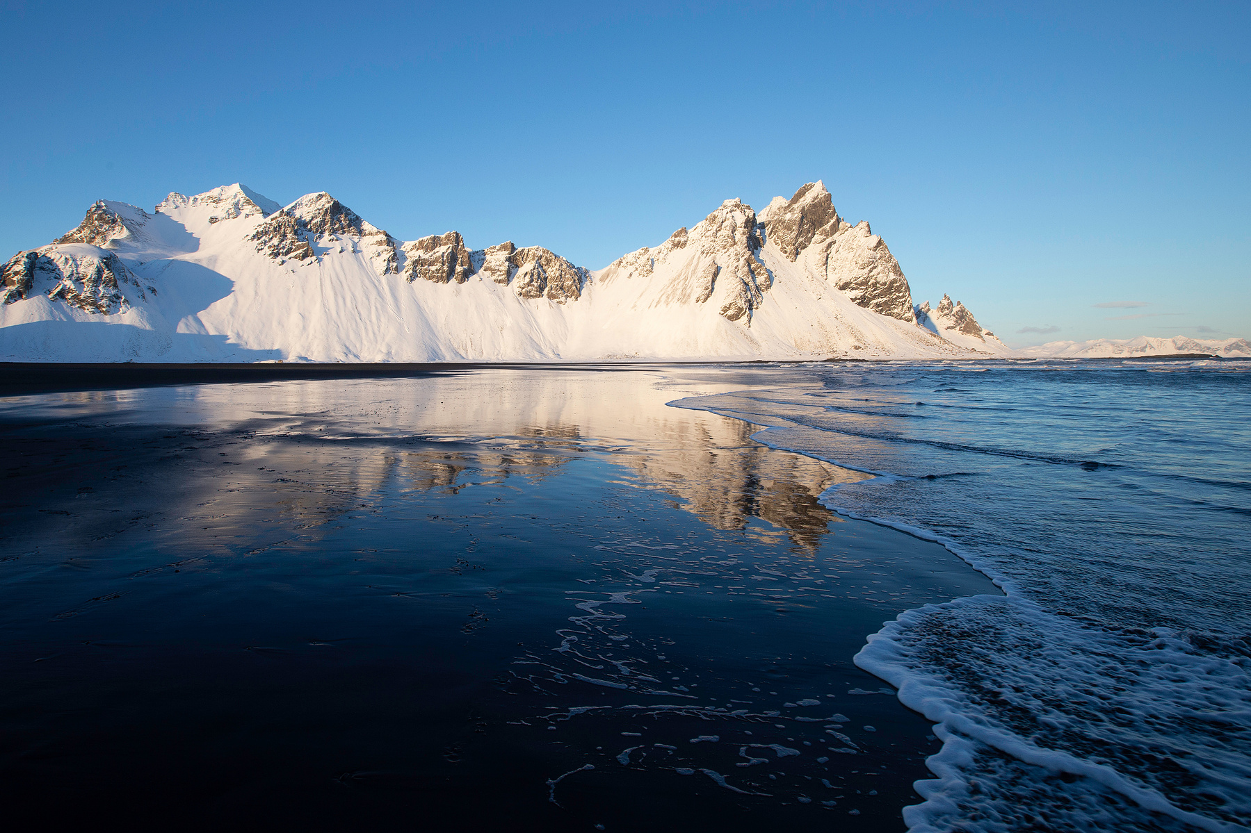 The magnificent Vestrahorn Mountain in Iceland is reflected on the wet black sand beach on a winter afternoon. (Landscape)