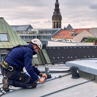Höhenarbeiter auf Dach, schraubt Sekurant fest. Sonnenuntergang in Magdeburg.