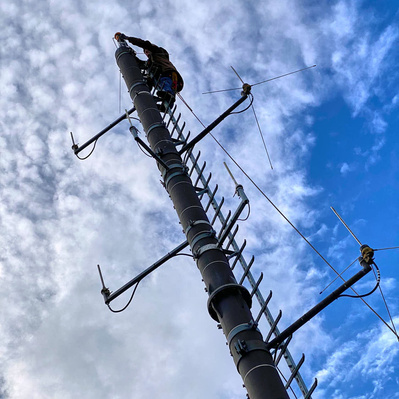 Höhenarbeiter befestigt Bauteil an einen Sendemast ohne Steiger, mit seiner Klettertechnik.