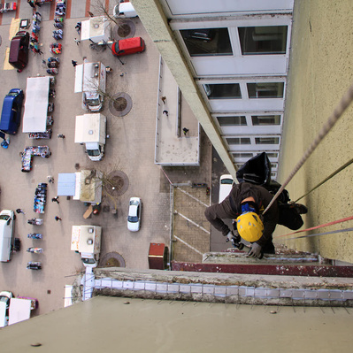 Höhenarbeiter hängt mit Seilen an Fase und bringt Taubenabwehr an. Es handelt sich um ein Hochhaus. Plattenbau.