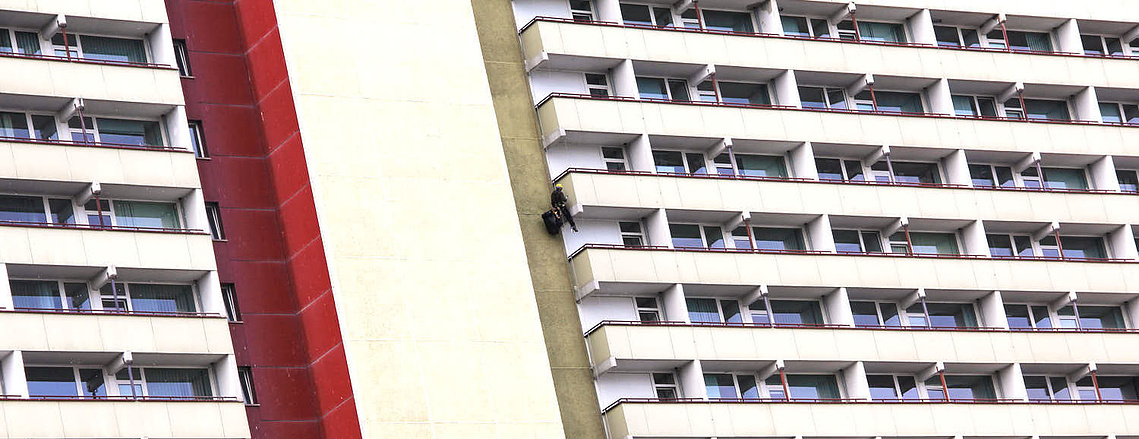 Hausfasade, Neubau, Kletterer hängt an der Fassade und begutachtet Balkone.